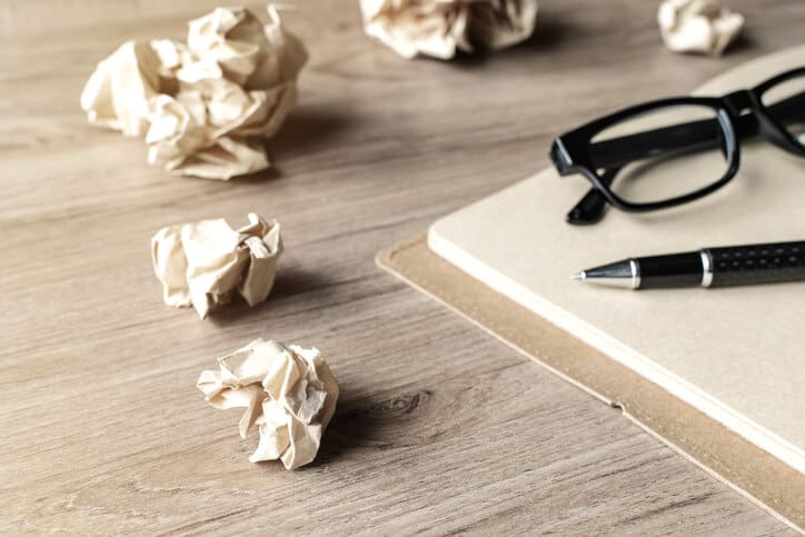 Crumpled paper balls with eye glasses and notebook on wood desk with soft light